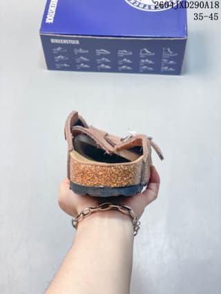 Rear view of a brown closed-toe clog with a textured outsole, shown in front of its shoe box.