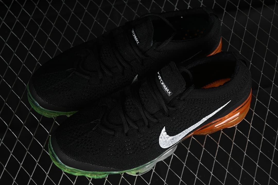 Pair of black VaporMax sneakers with white Swooshes and green-to-orange transparent soles.