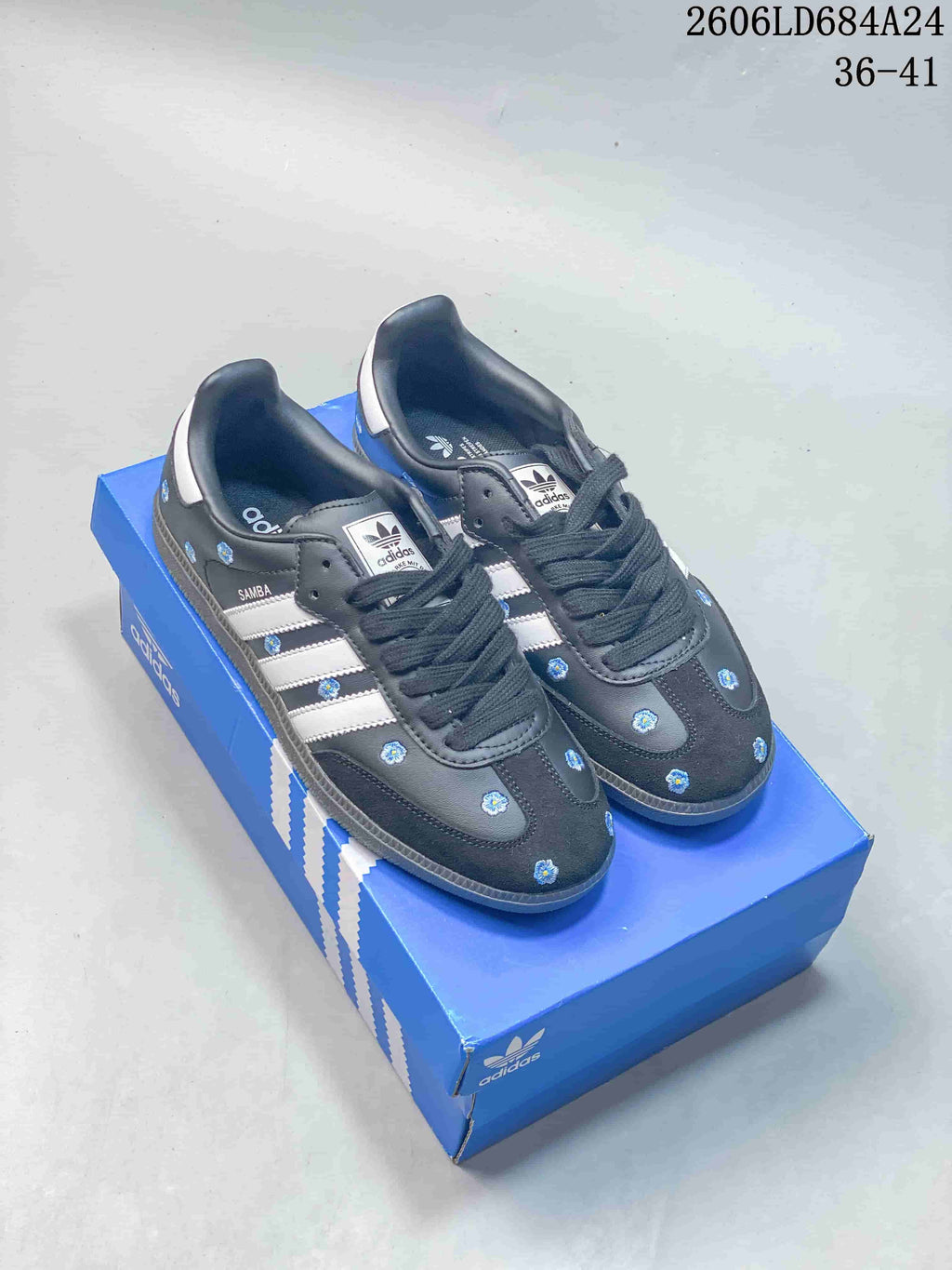 Charcoal Adidas Samba sneakers with blue floral details and white side stripes.