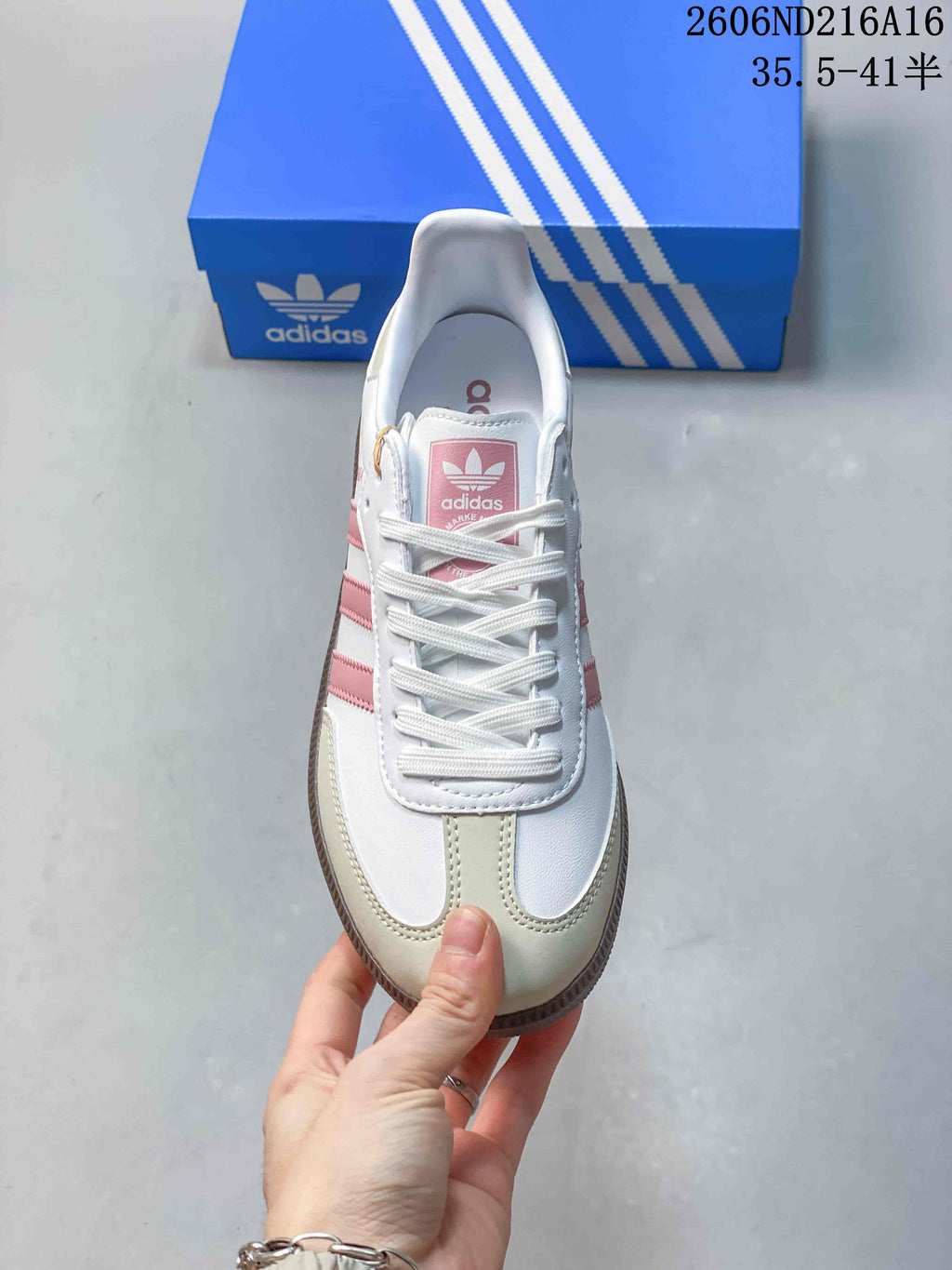 Front view of a white low-top sneaker with pink stripes, white laces, and pale neutral toe overlays
