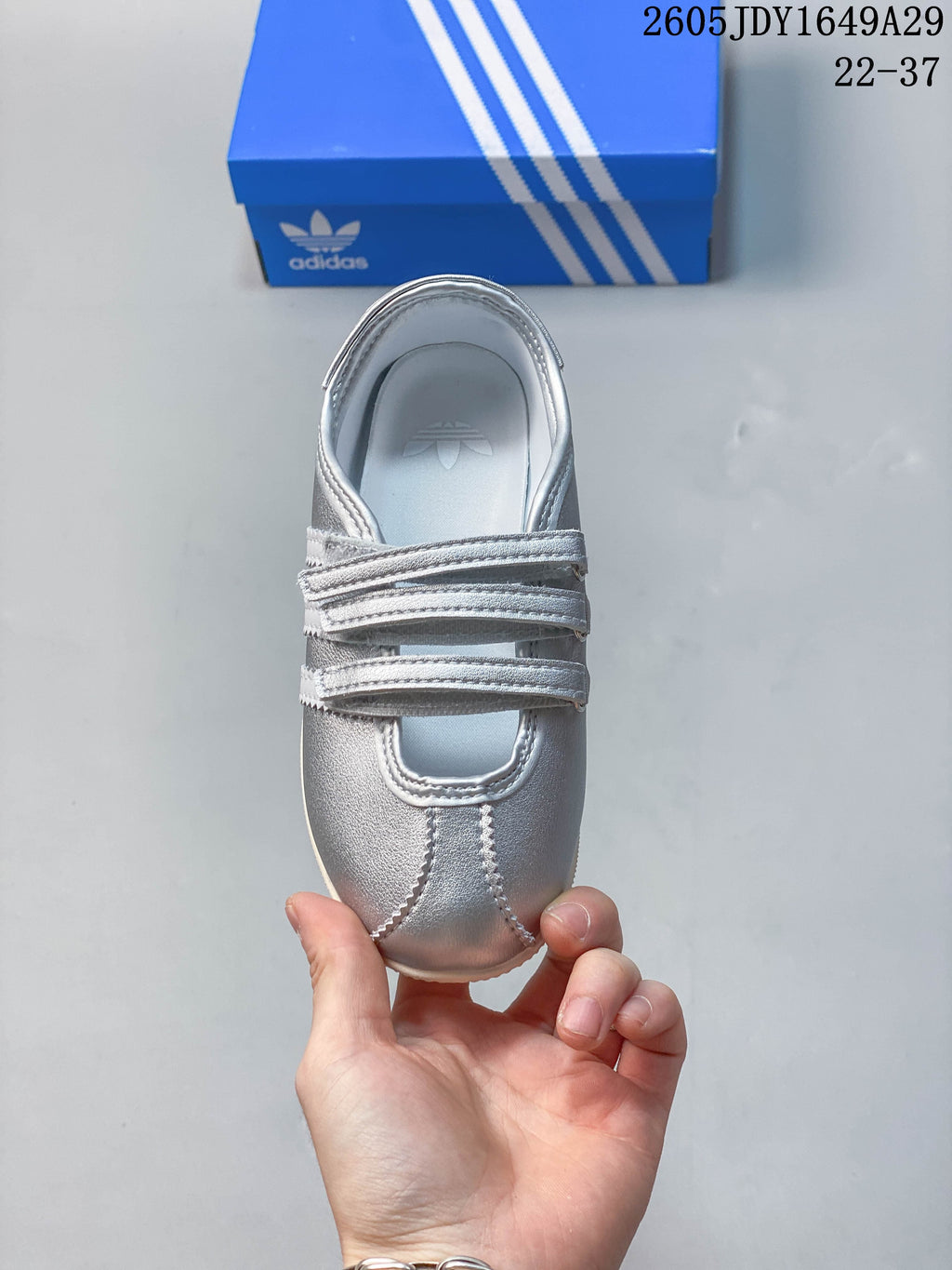Top view of a silver sneaker showing the hook-and-loop straps and stitched toe panels