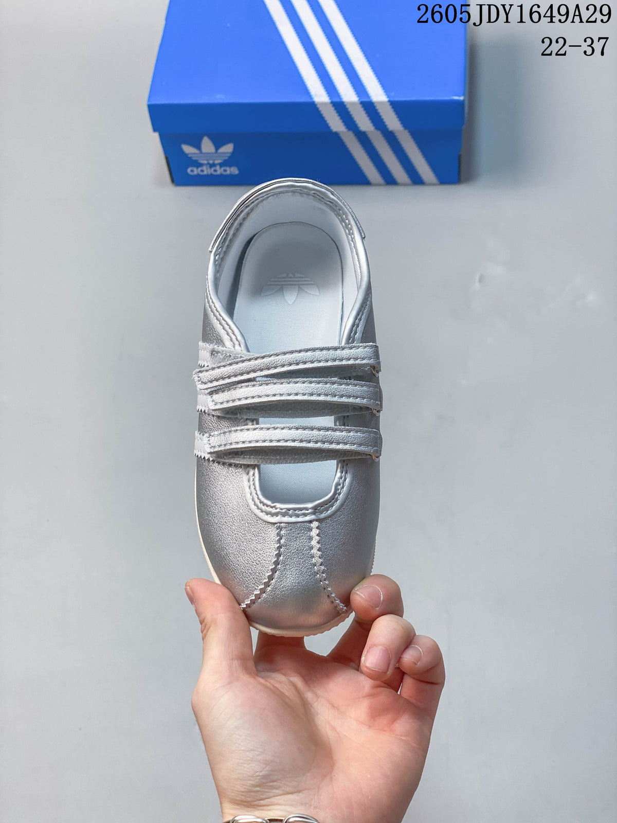 Top view of a silver sneaker showing the hook-and-loop straps and stitched toe panels