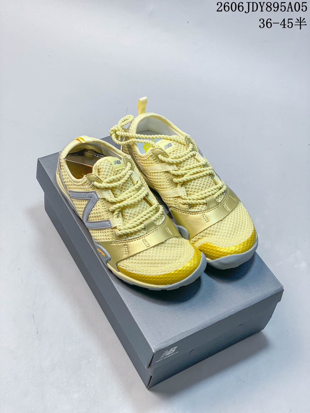 Pair of pale yellow and gold-toned New Balance MT10O sneakers displayed on a box