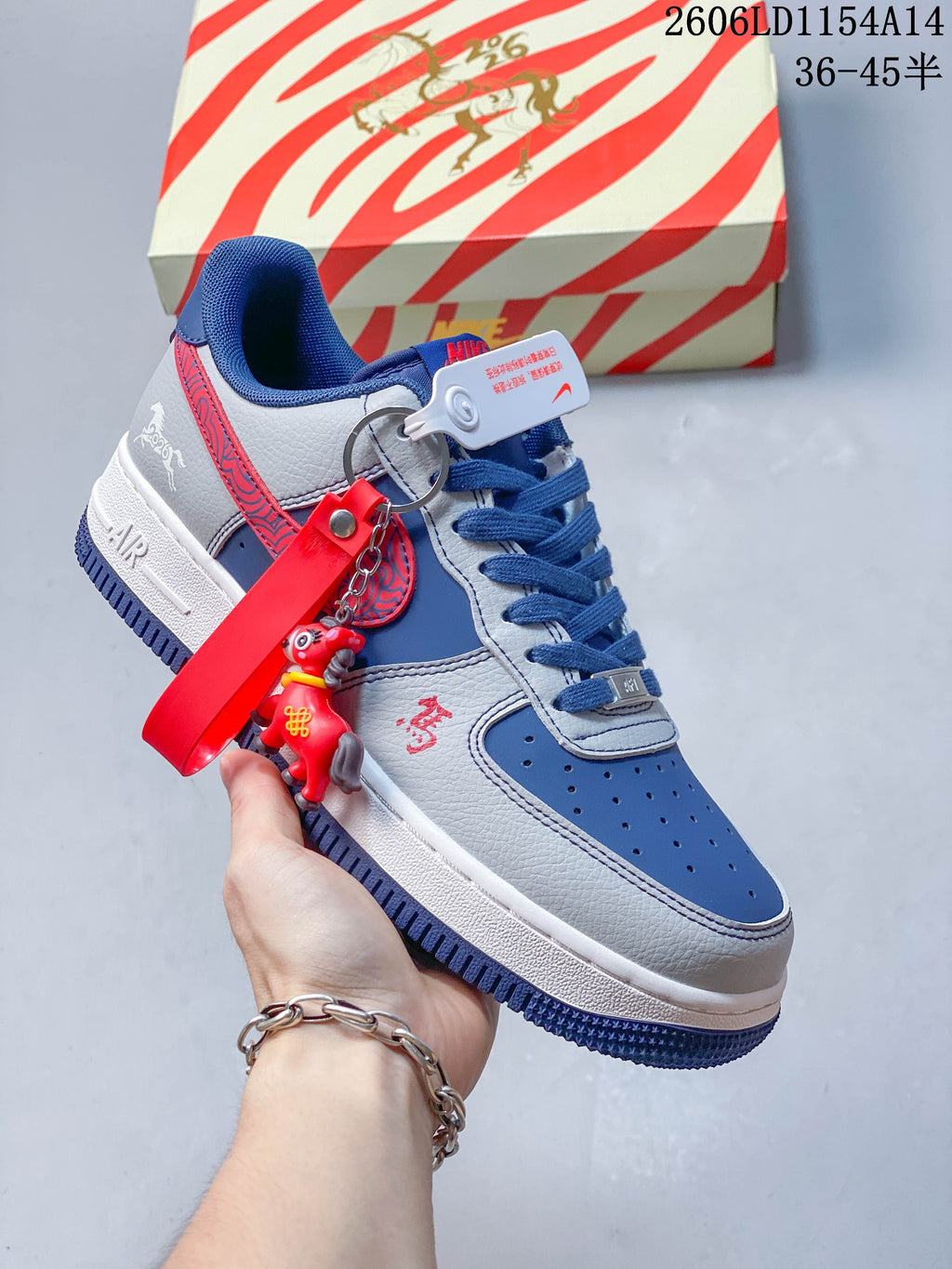 Blue and light gray low-top sneaker with contrasting panels, blue laces and a red charm