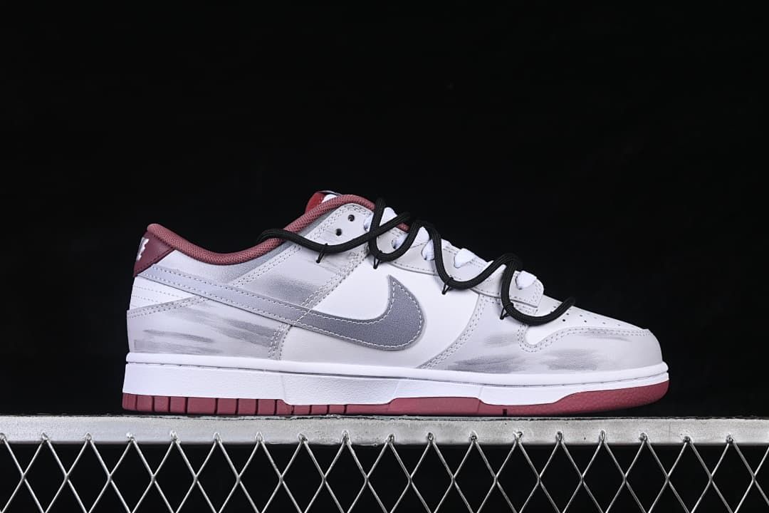 Side profile of a white low-top sneaker with gray overlays, burgundy outsole, and black cord-style straps