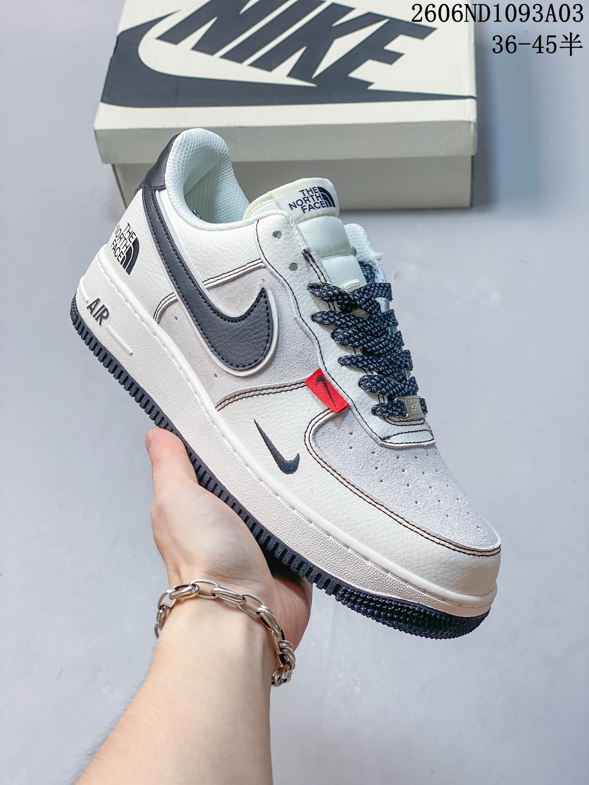 Close side view of a white sneaker with dark gray accents and a red tab
