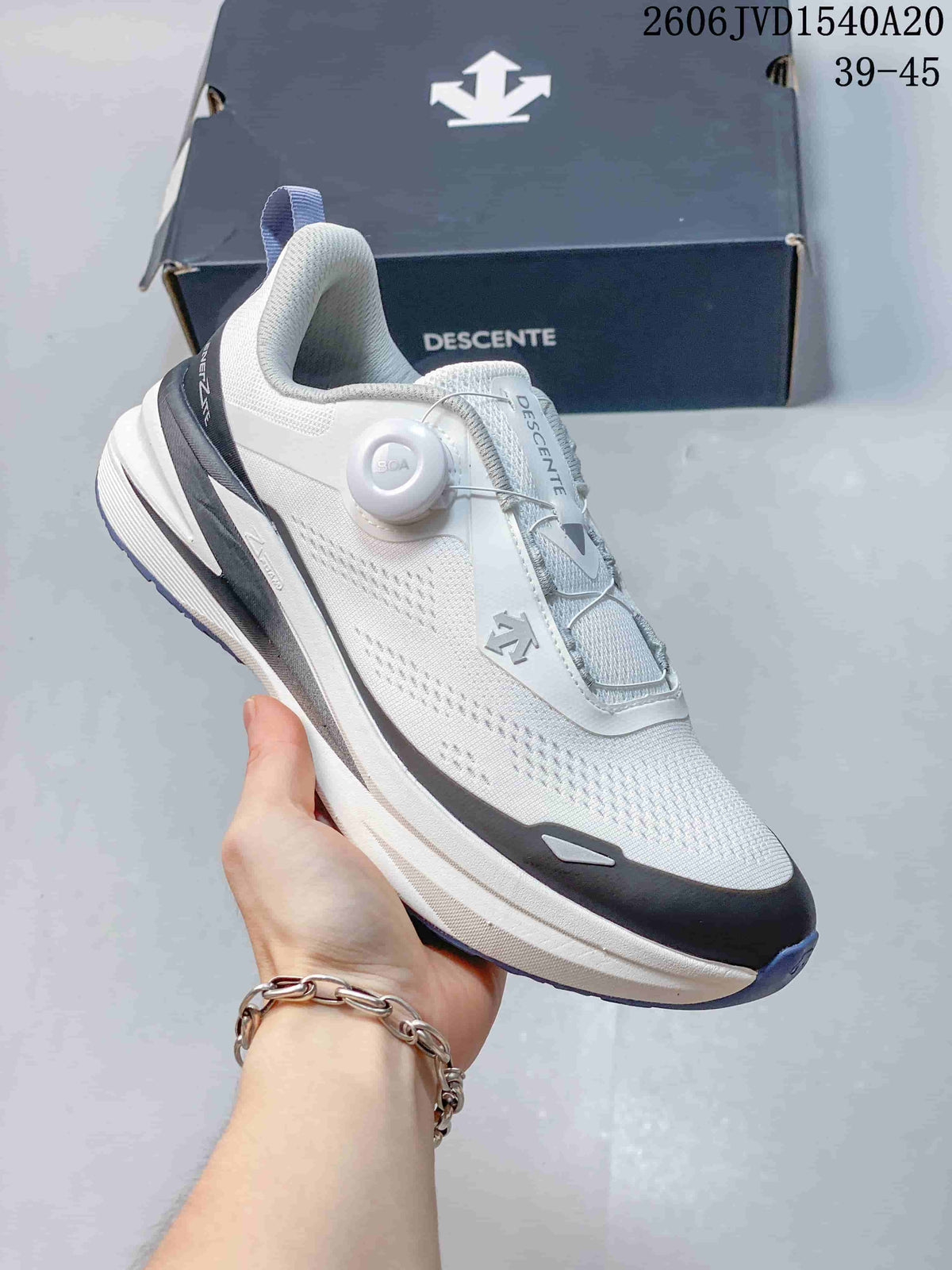Angled side view of a white and gray DESCENTE sneaker with dial-style closure