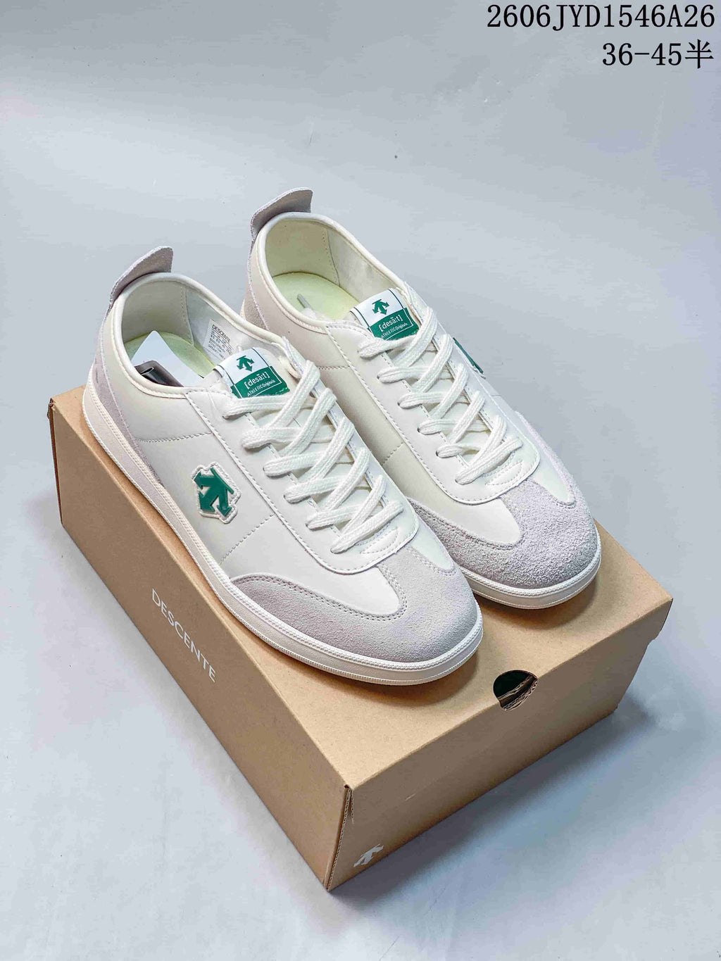 White sneakers with pale gray overlays and green accents displayed on a shoe box.