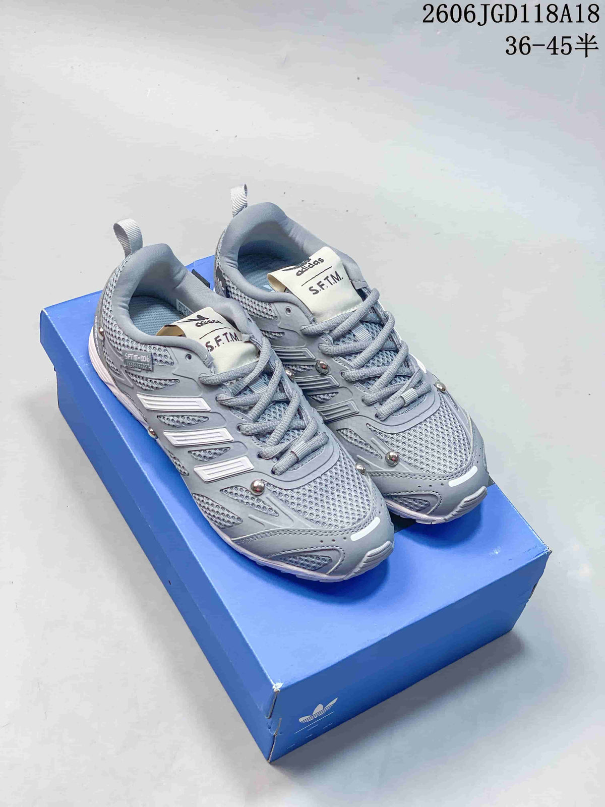 Pair of grey Song for the Mute x adidas Adizero PR SFTM sneakers on a blue box