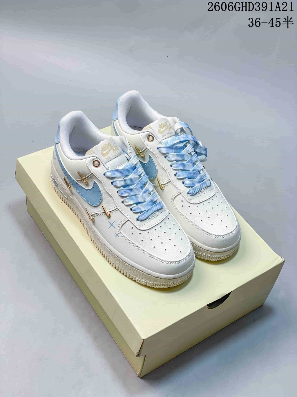 Pair of white low-top sneakers with light-blue Swoosh accents, patterned laces and gold-tone details.