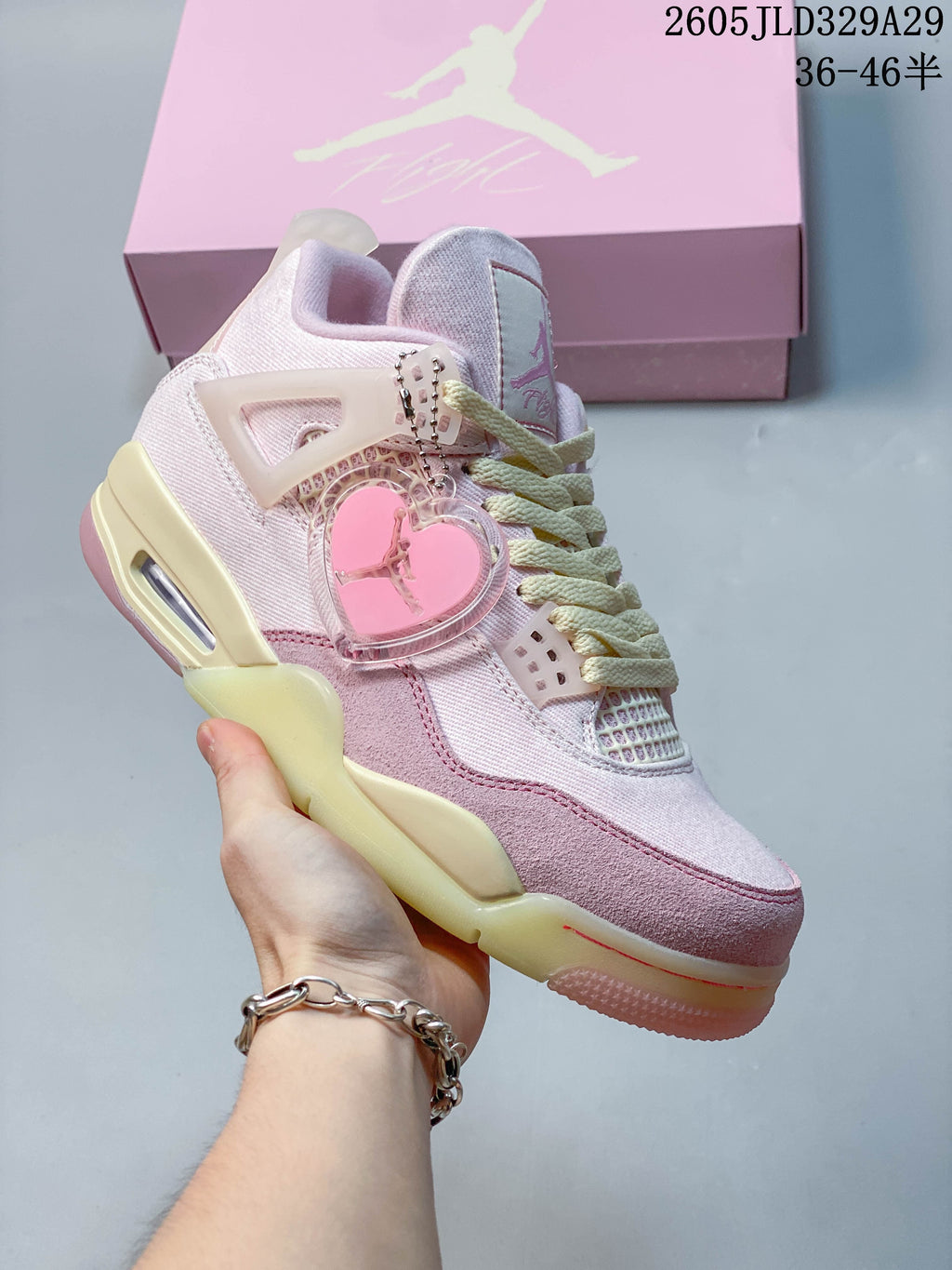 Side view of a pink Jordan Air Jordan 4-style sneaker with pale laces and a heart-shaped accessory.