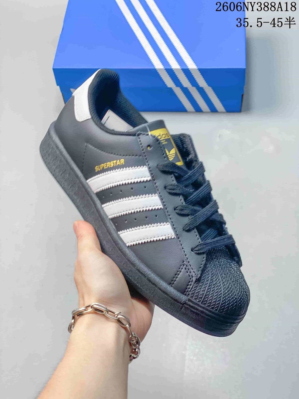 Angled view of a dark gray Adidas Superstar-style sneaker with white stripes and a shell toe; image overlay reads “35.5–45.5.”