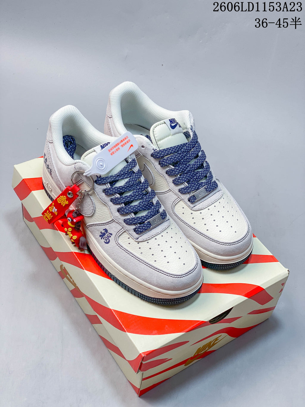 Pair of white and pale gray Nike Air Force 1 '07 low-top sneakers with dark blue laces and a red charm