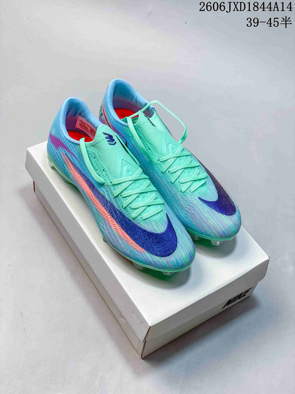 Pair of mint and aqua Nike Mercurial soccer cleats with blue and coral accents on a shoebox.