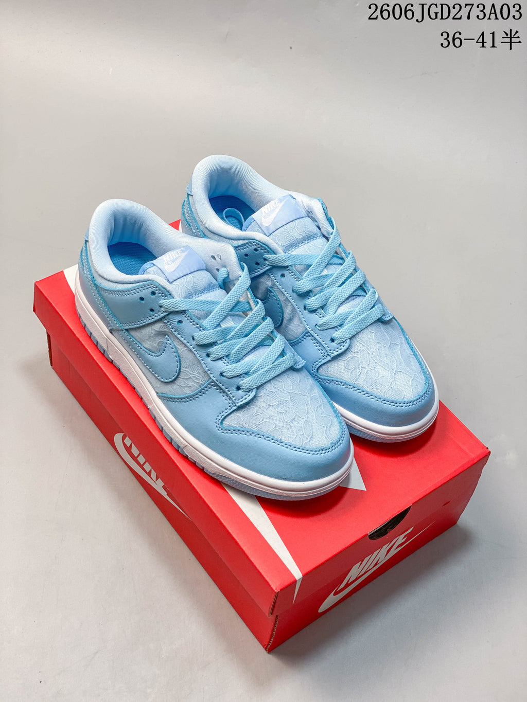 Pair of light blue and white low-top sneakers with patterned panels, shown on a red shoe box