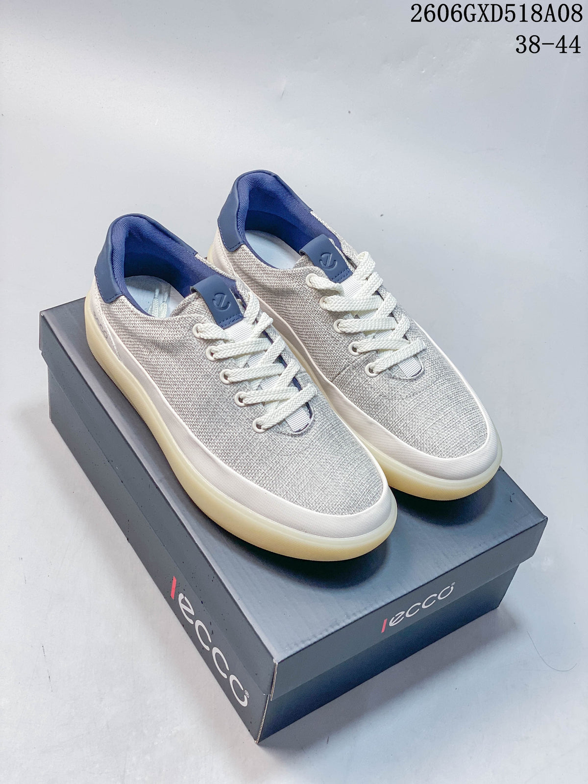 Pair of gray ECCO lace-up sneakers with blue heel and tongue accents, shown on a branded box; image displays style code 2606GXD518A08 and sizes 38–44.