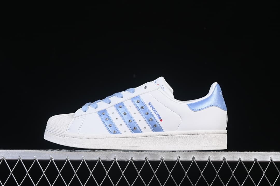 Side view of a white adidas Superstar II sneaker with pale blue stripes, laces, and heel accent.