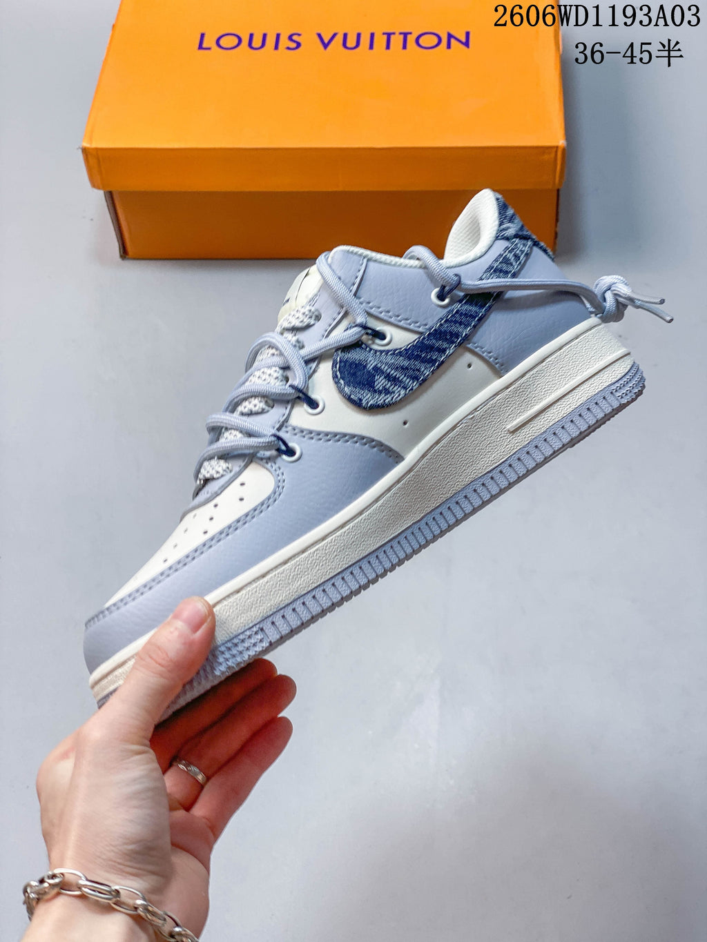 Side profile of the low-top sneaker showing pale gray overlays, a blue patterned side panel, and a light-colored sole.