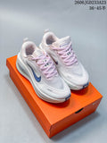 Pair of white Nike Vomero Plus shoes with pale pink laces and blue Swoosh details, shown on an orange shoe box.