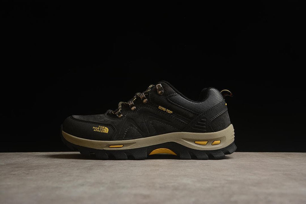 Side profile of a black The North Face hiking shoe with yellow details and a beige midsole.