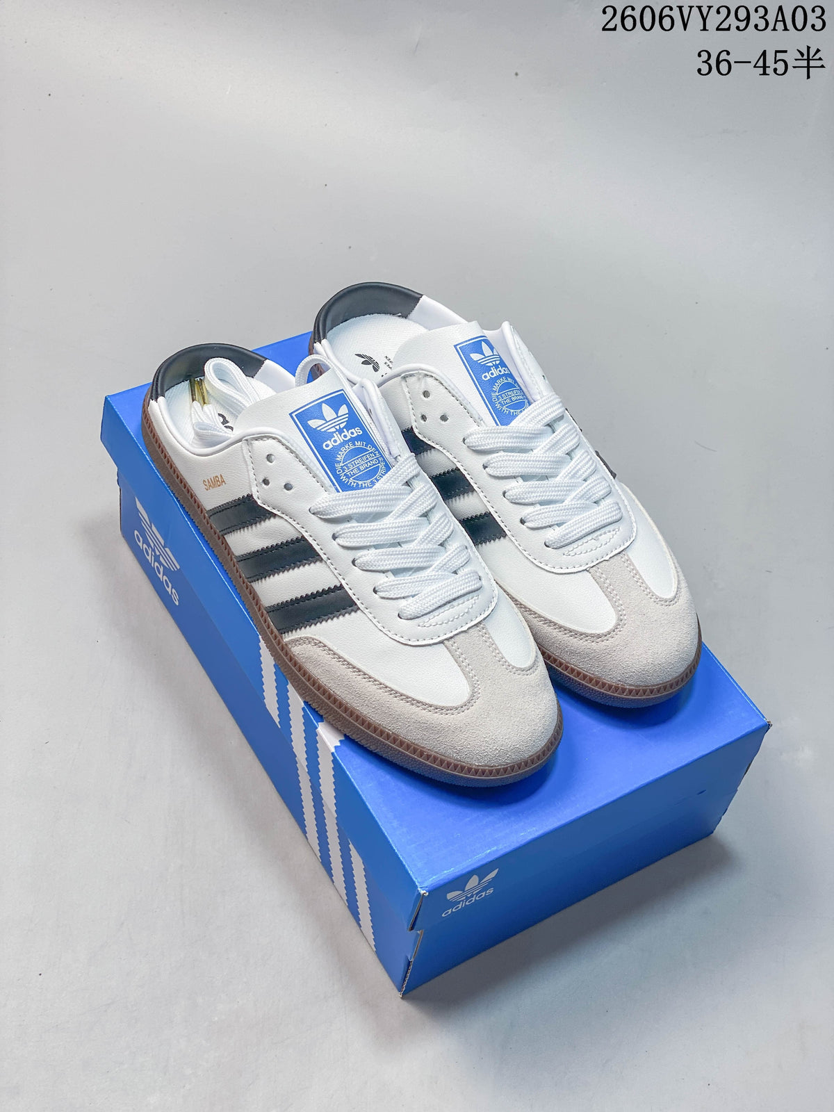 White Adidas low-top sneakers with dark stripes and gum-colored soles on a blue shoe box.