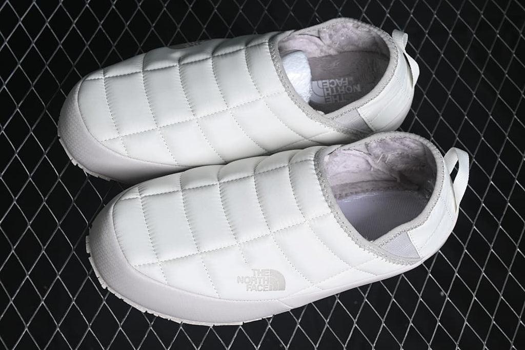 Pair of white quilted mule slippers viewed from above.