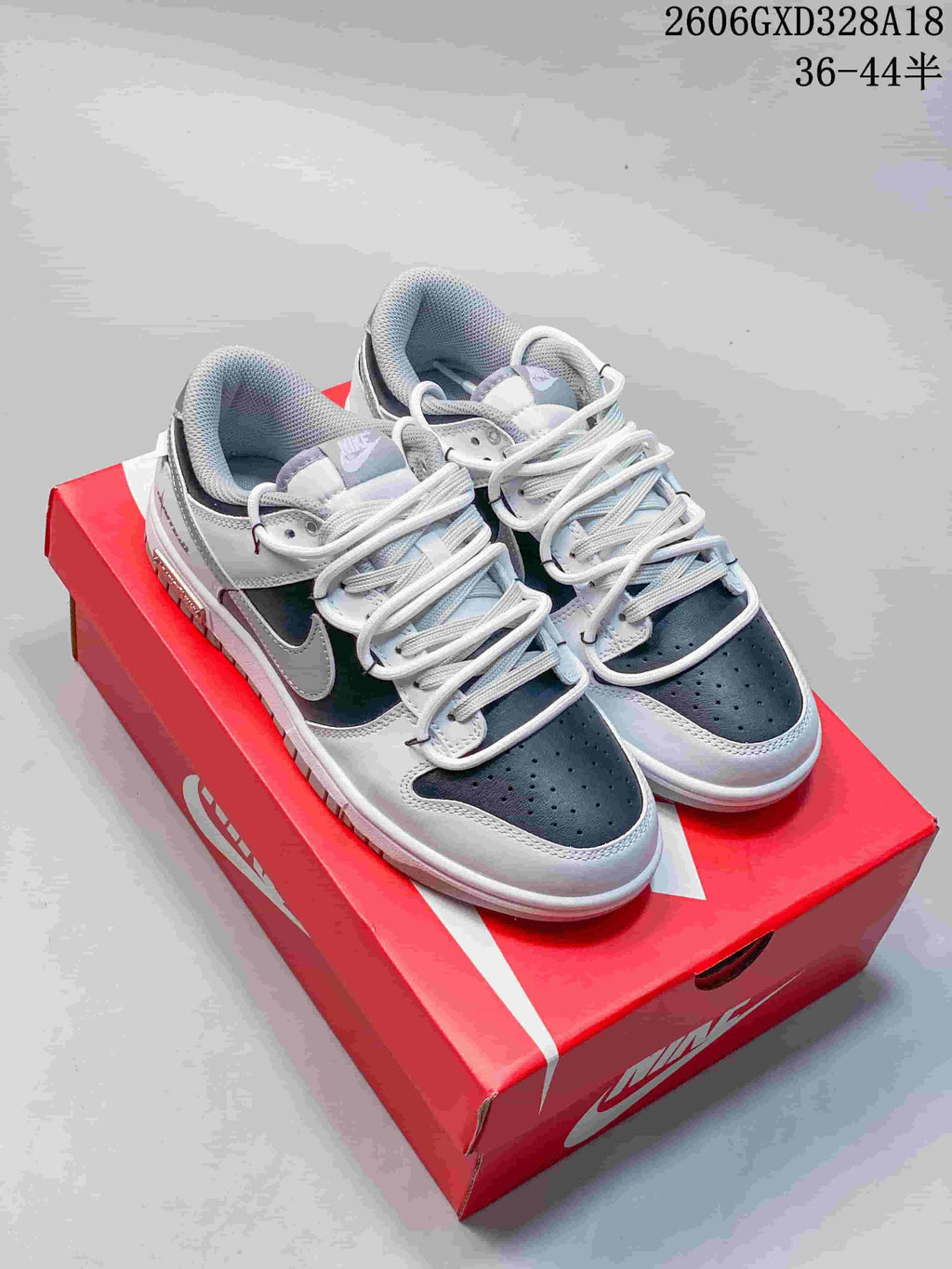 Pair of white, black, and silver low-top sneakers displayed on a red shoe box
