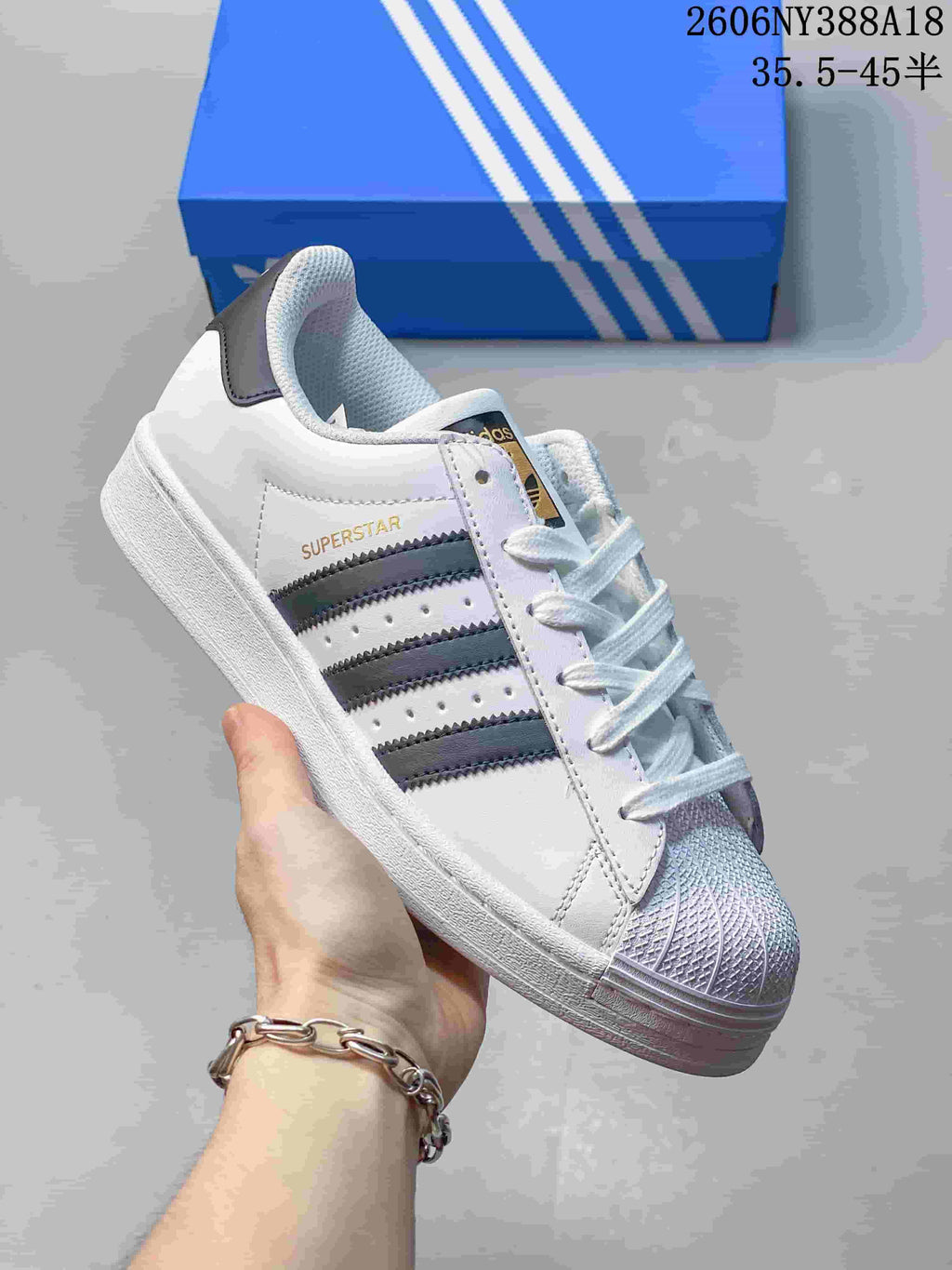 Close-up of a white Adidas Superstar sneaker with dark side stripes and a textured shell toe.