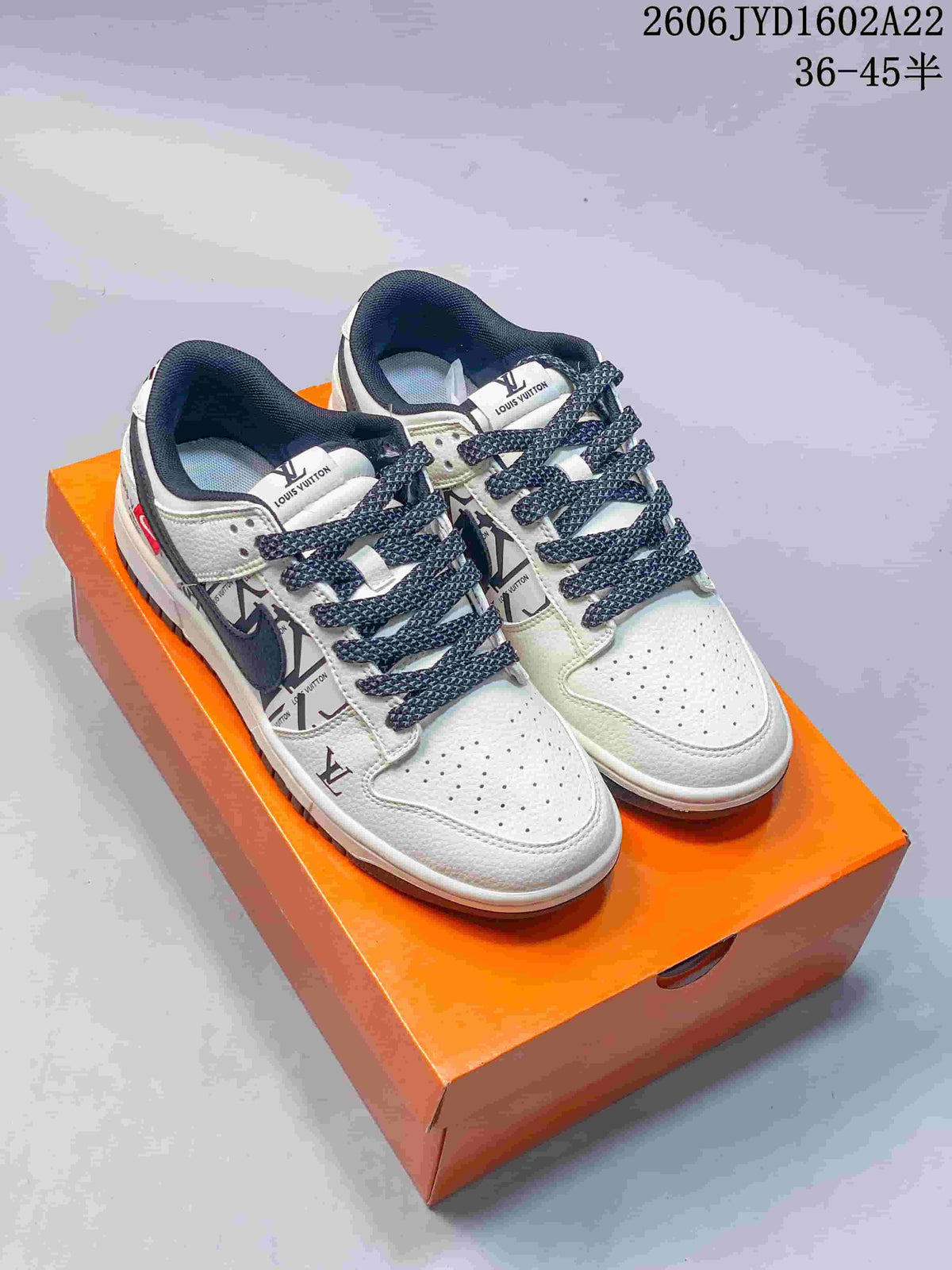 Pair of white and navy low-top sneakers with patterned side panels displayed on an orange box