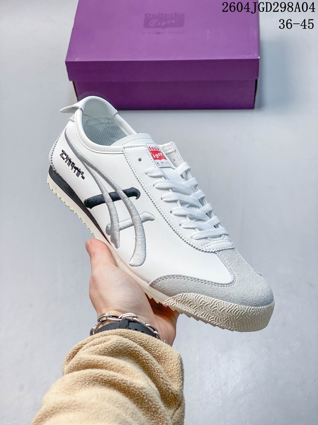 White Onitsuka Tiger Mexico 66 Deluxe sneaker with silver and dark accents, shown beside a purple shoe box.