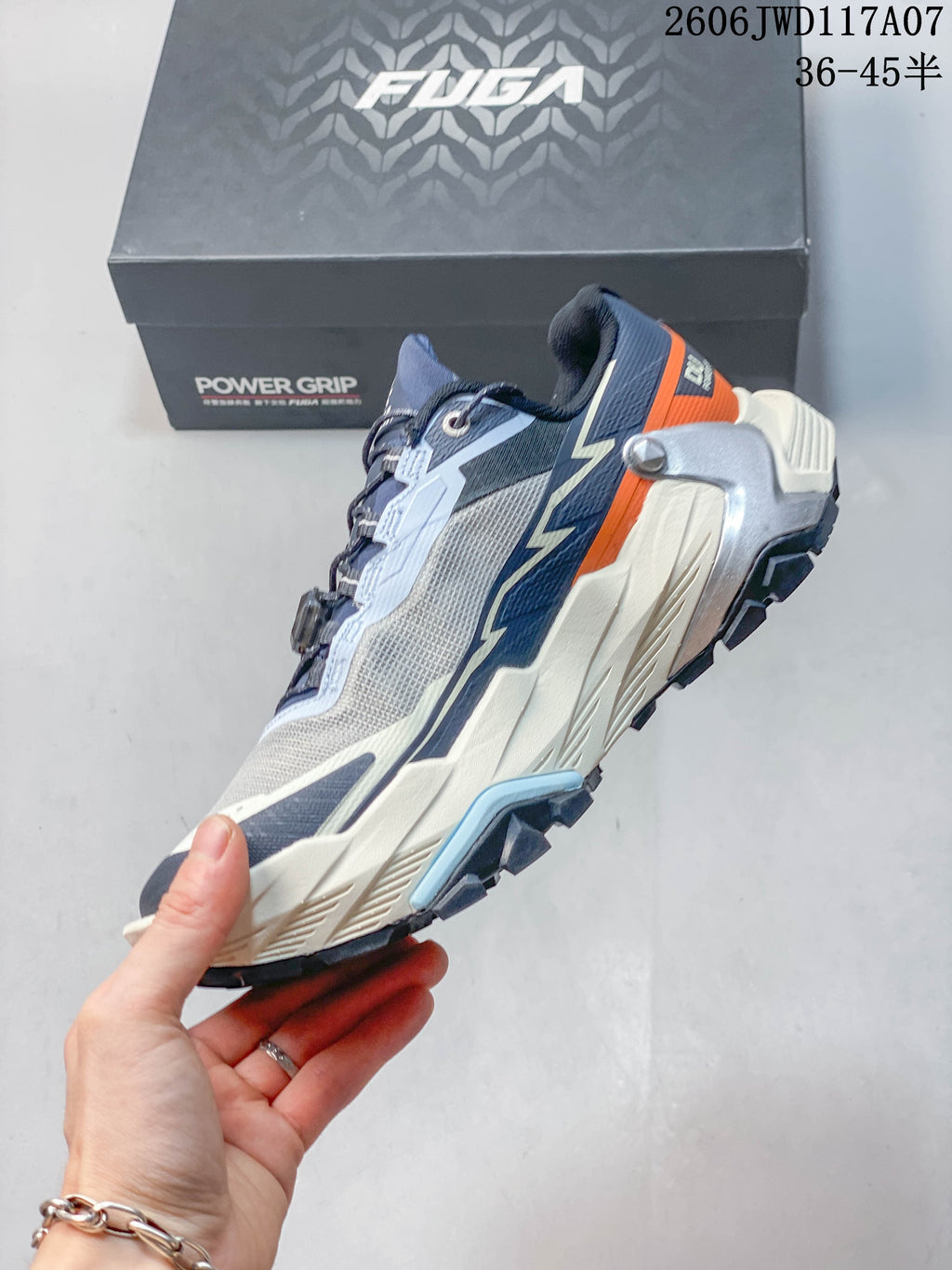 Side view of the trail running shoe with gray, navy, pale blue, cream, and orange details