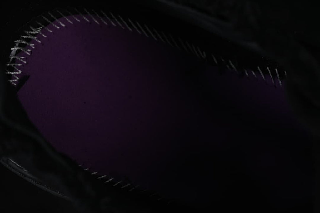 Dark close-up of a purple-toned shoe component with visible stitching