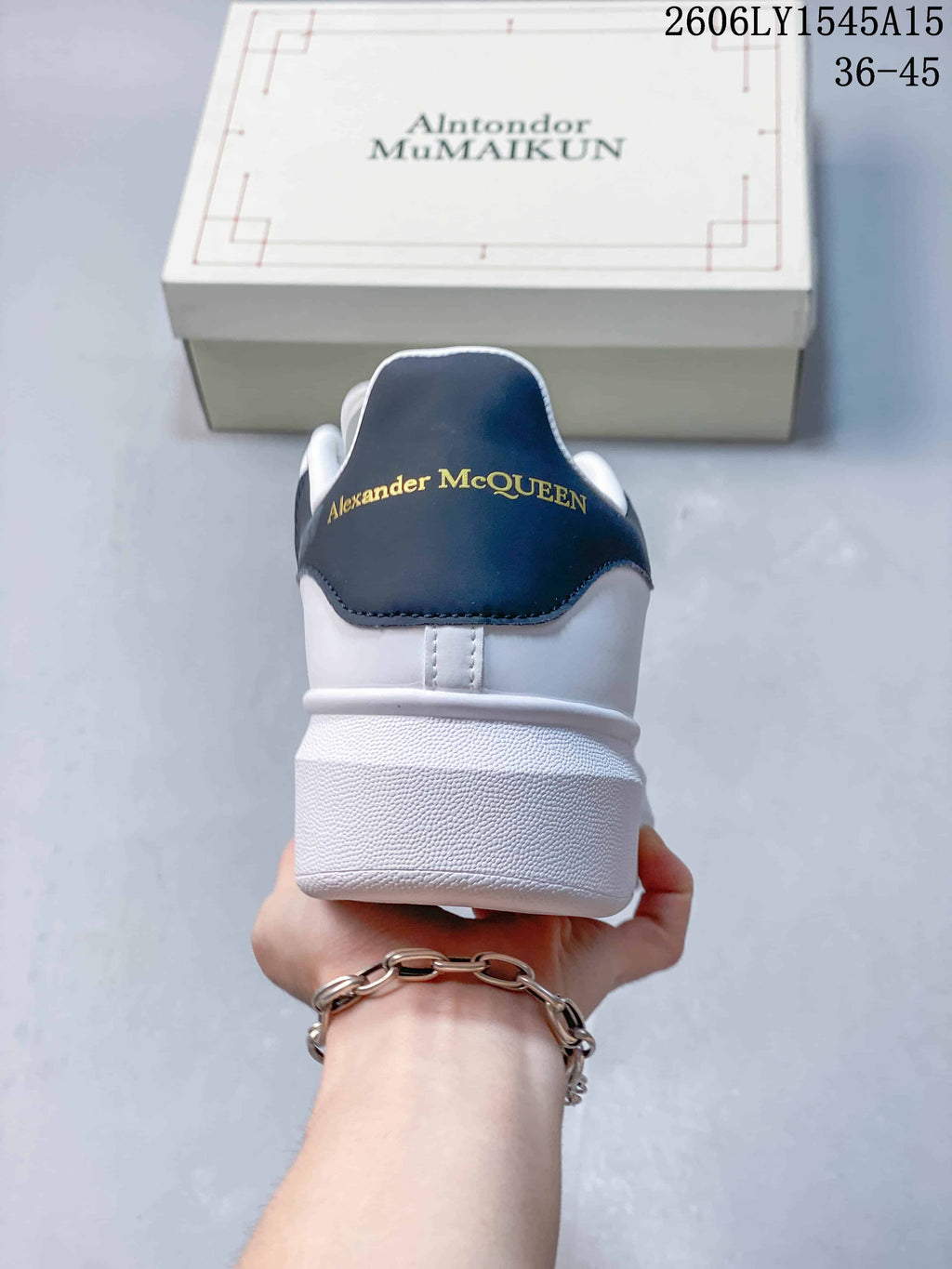 Rear view of a white sneaker with a navy heel tab and gold-tone lettering.