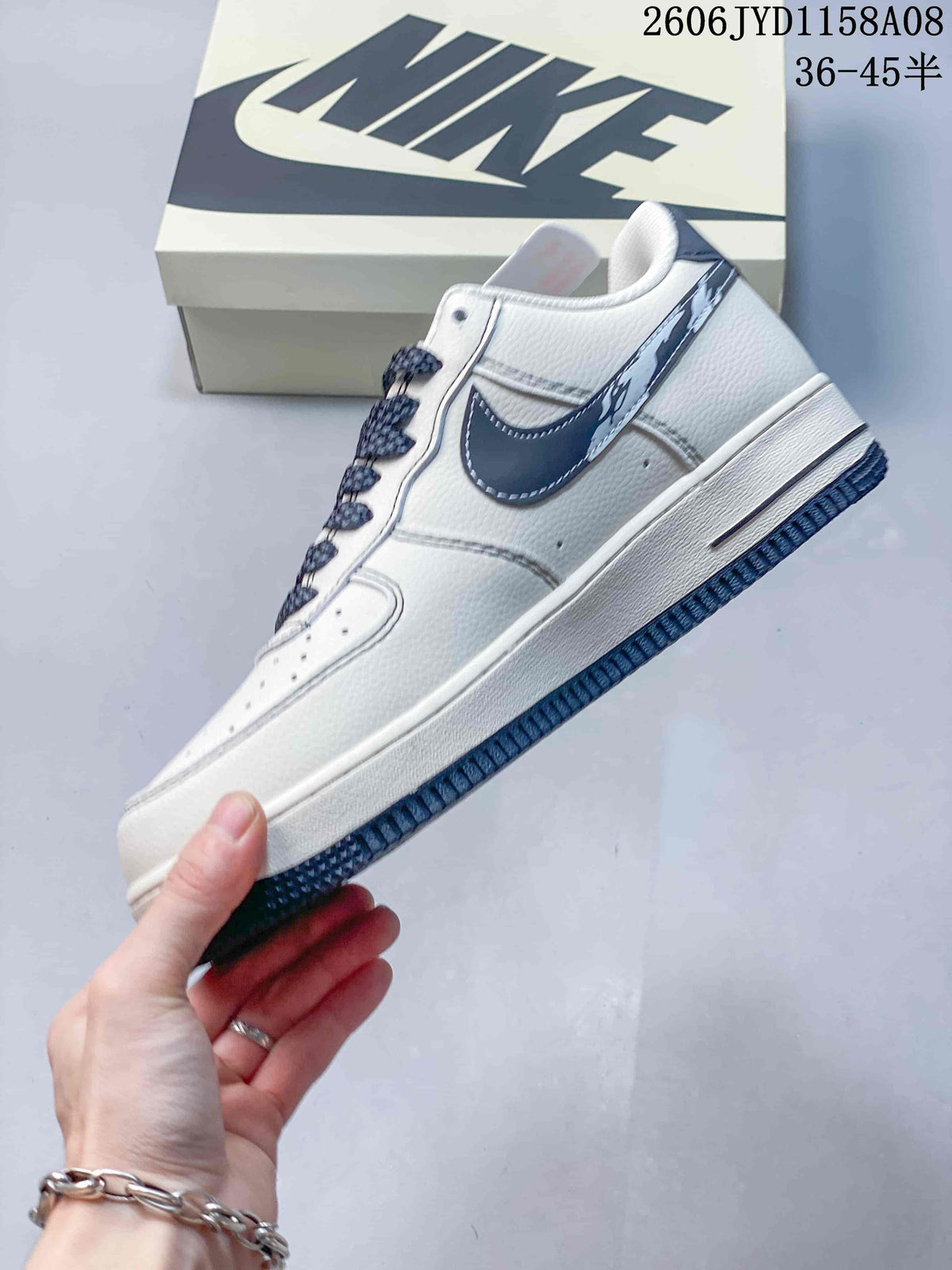 Side view of the white low-top sneaker with navy Swoosh, patterned laces, and navy outsole.