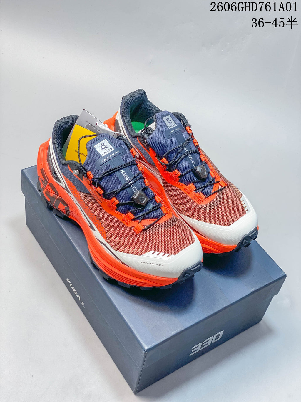 Pair of Kailas FUGA EX330 trail shoes in rust red, bright orange, navy, and white, shown on a shoe box
