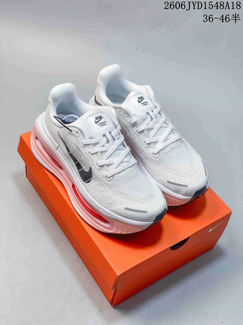 Pair of white Nike Vomero Premium running shoes with pink midsole accents, shown on an orange shoe box.
