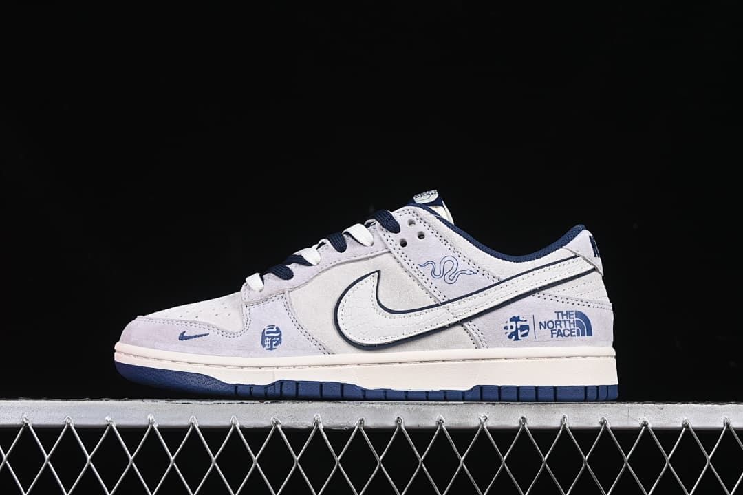 Side view of light gray and white Nike SB Dunk Low sneakers with navy accents and Snake Year graphics.