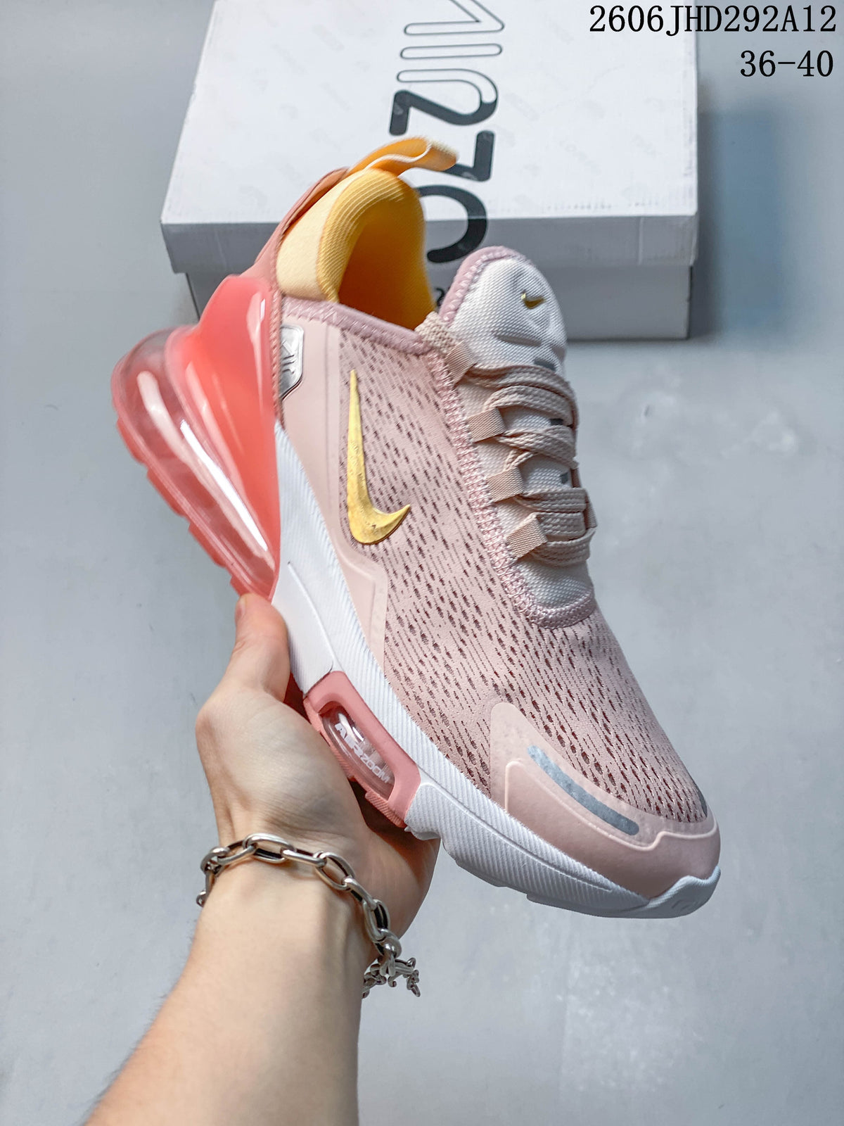 Side view of a pale pink Nike Air Max 270-style sneaker with gold accents and a coral heel unit.