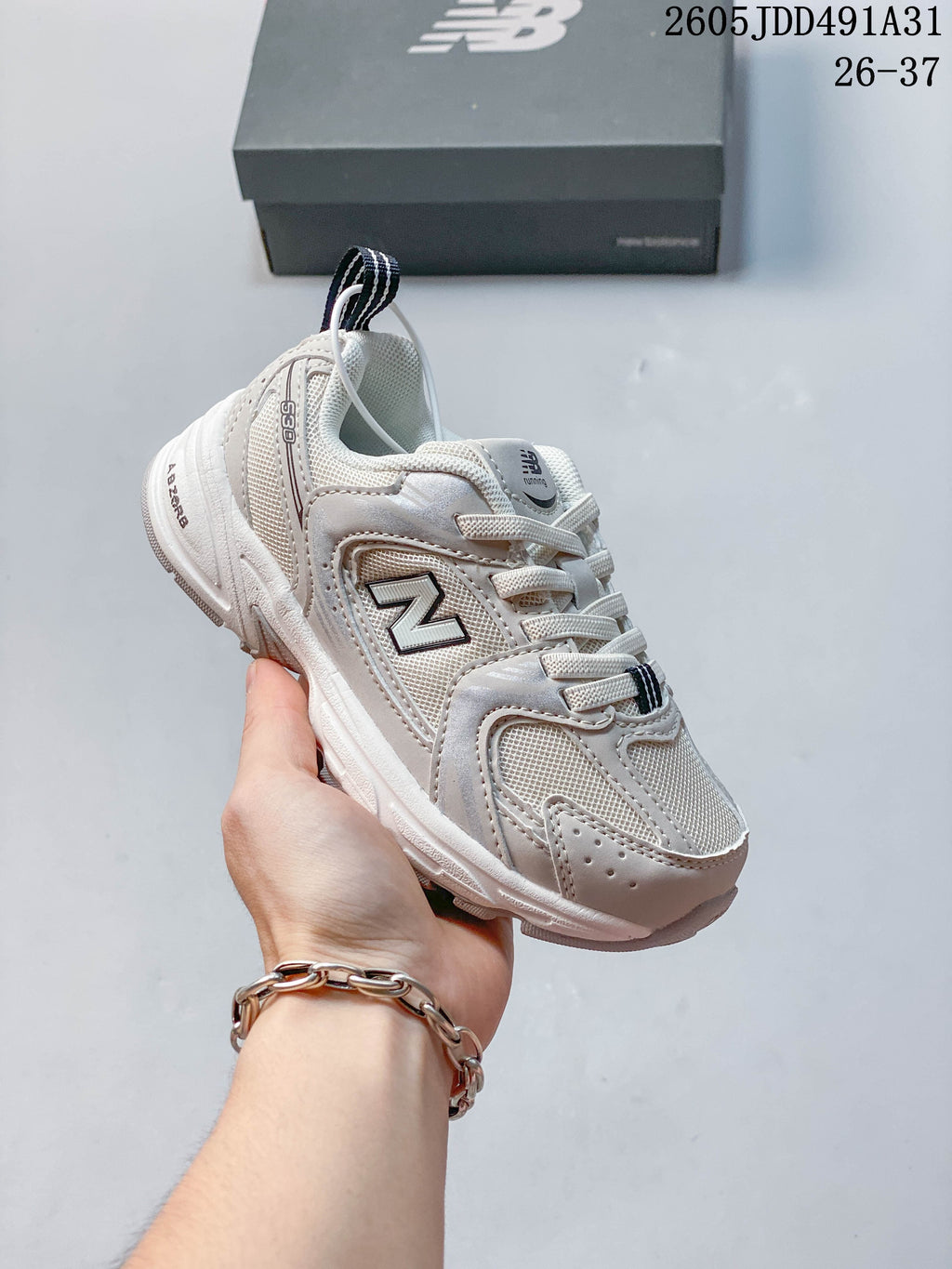 Light-colored kids' New Balance 530 lace-up sneaker with dark details, shown in hand.