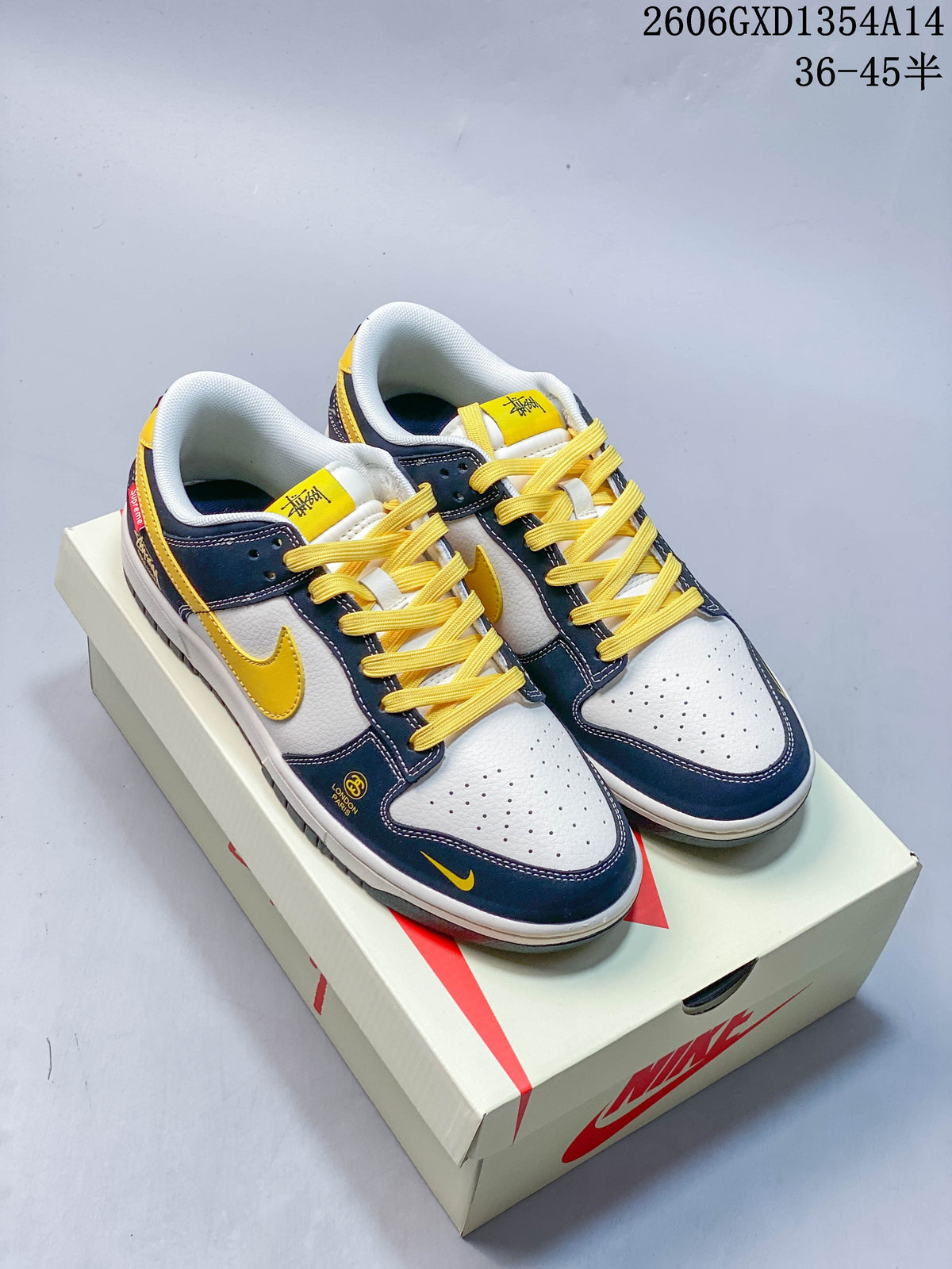 Pair of white and navy Nike Dunk Low sneakers with yellow laces and accents