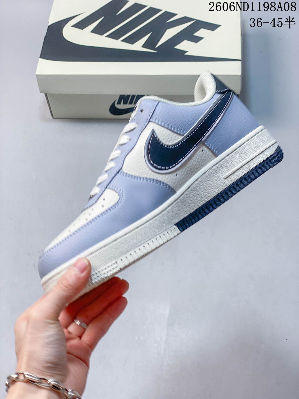 Side view of the light-blue and off-white low-top sneaker with a dark Swoosh panel, white midsole, and dark outsole; image overlay shows code 2606ND1198A08 and size range 36–45.5.