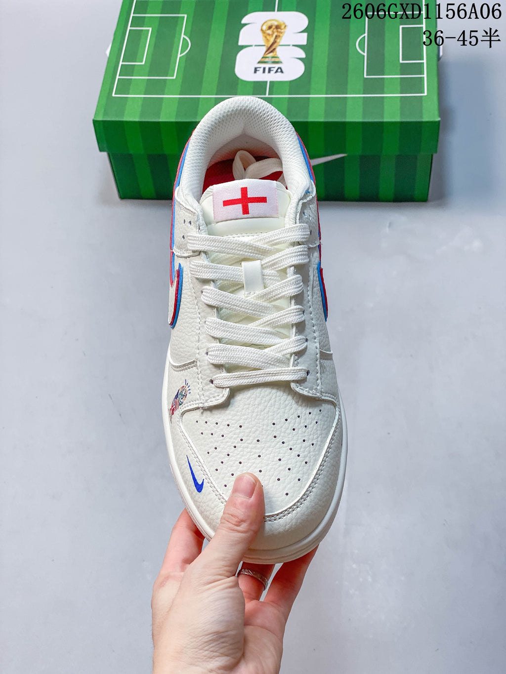 Top view of the sneaker showing white laces, perforated toe, and a red cross emblem on the tongue.