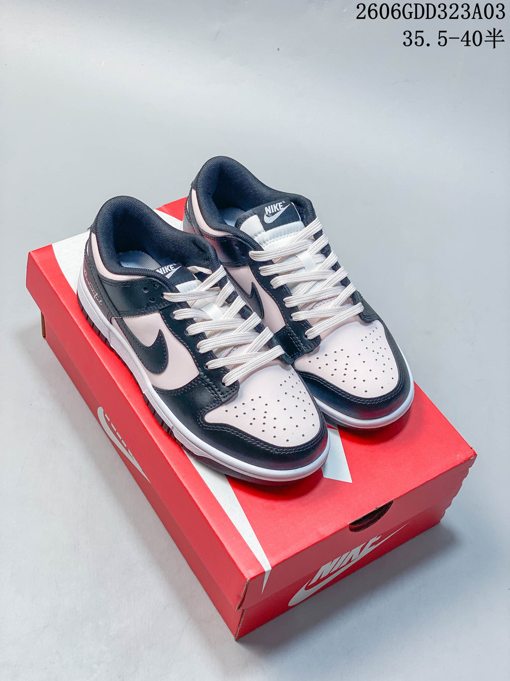Pair of black and pale pink Nike Dunk low-top sneakers displayed on a red shoebox