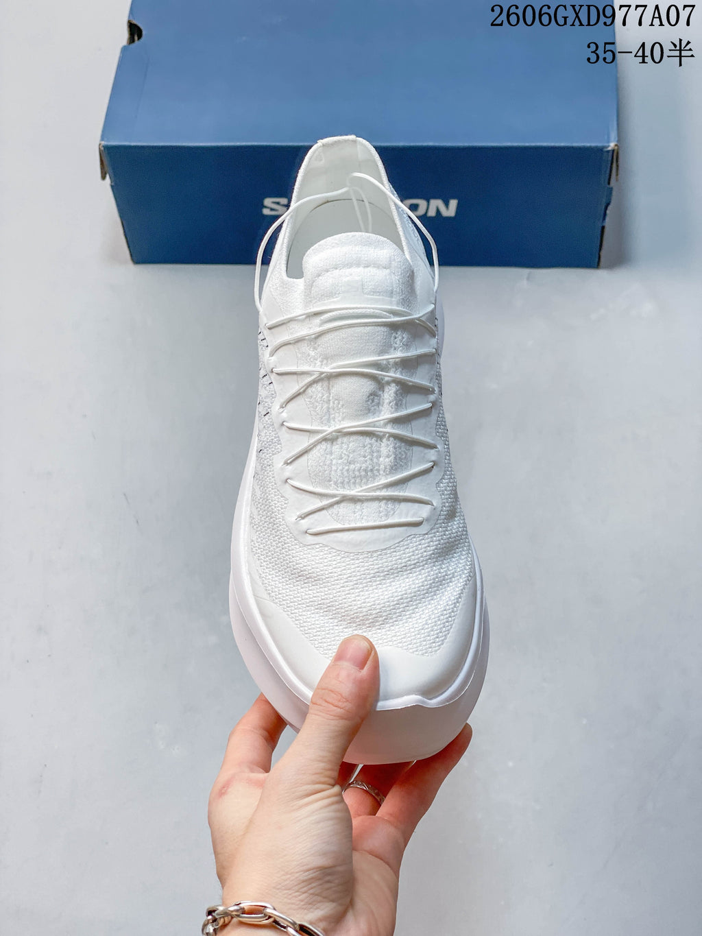 Front view of a white sneaker with cord-style lacing and a rounded toe.
