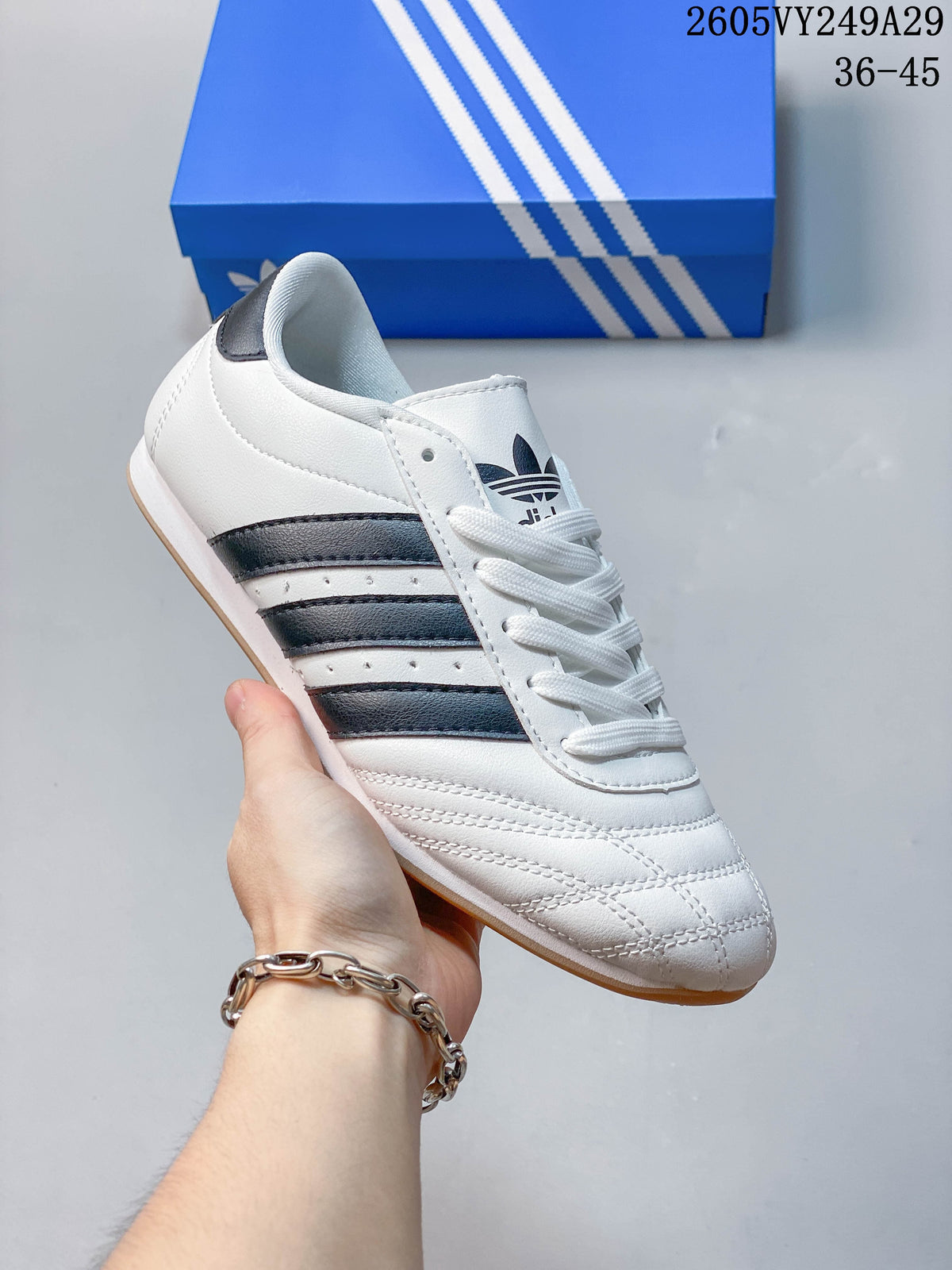 Close-up of a white low-top lace-up shoe with dark stripes and a light brown-toned outsole.