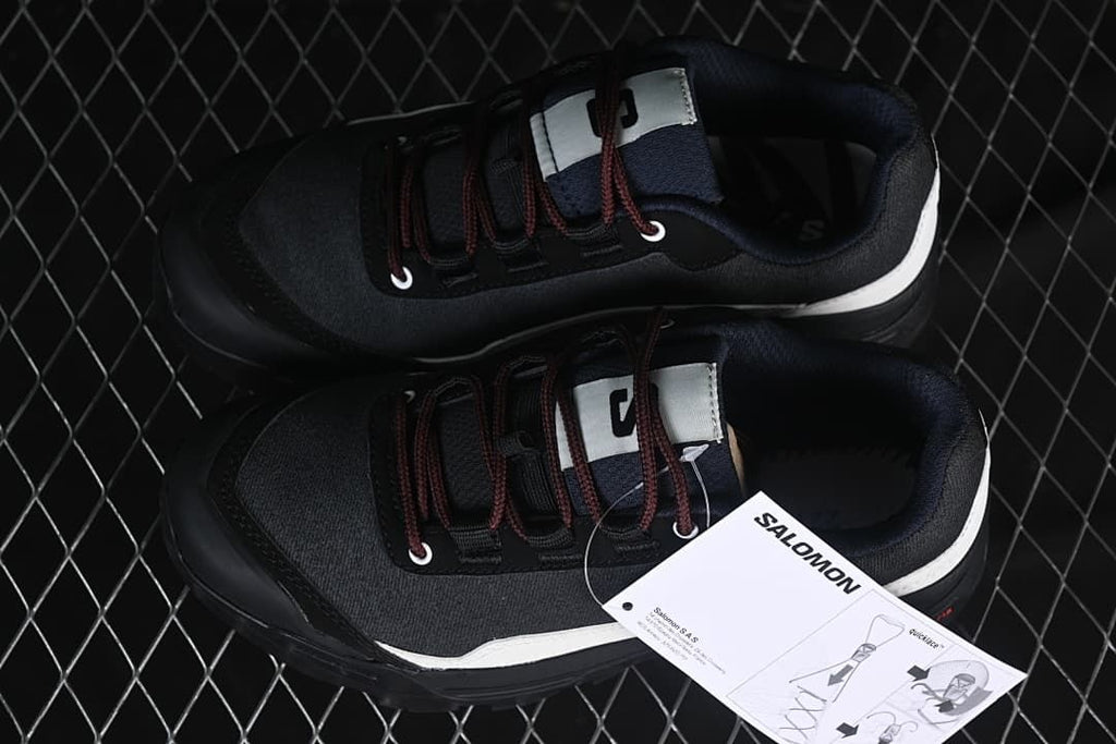 Pair of black and white Salomon shoes viewed from above beside a product tag.