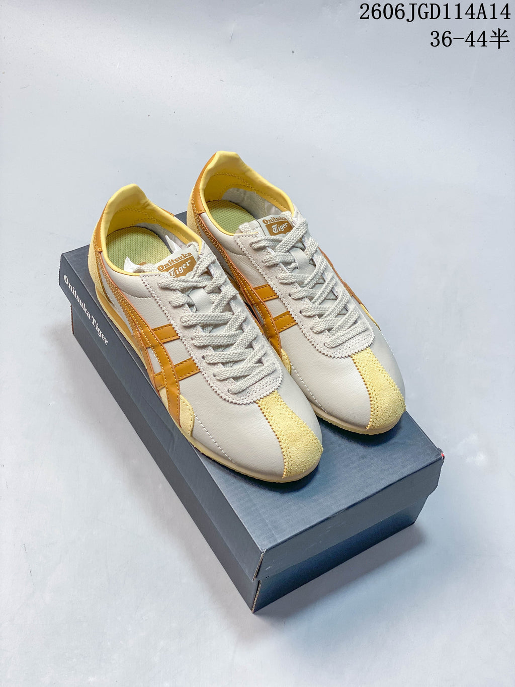 Pair of light neutral Onitsuka Tiger Runspark low-top sneakers with mustard-gold stripes, shown on a branded box