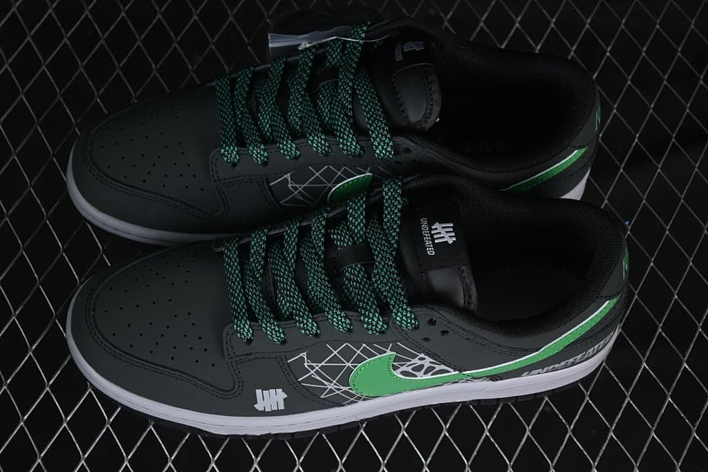 Overhead view of a pair of black low-top sneakers with green-and-black patterned laces and green Swooshes