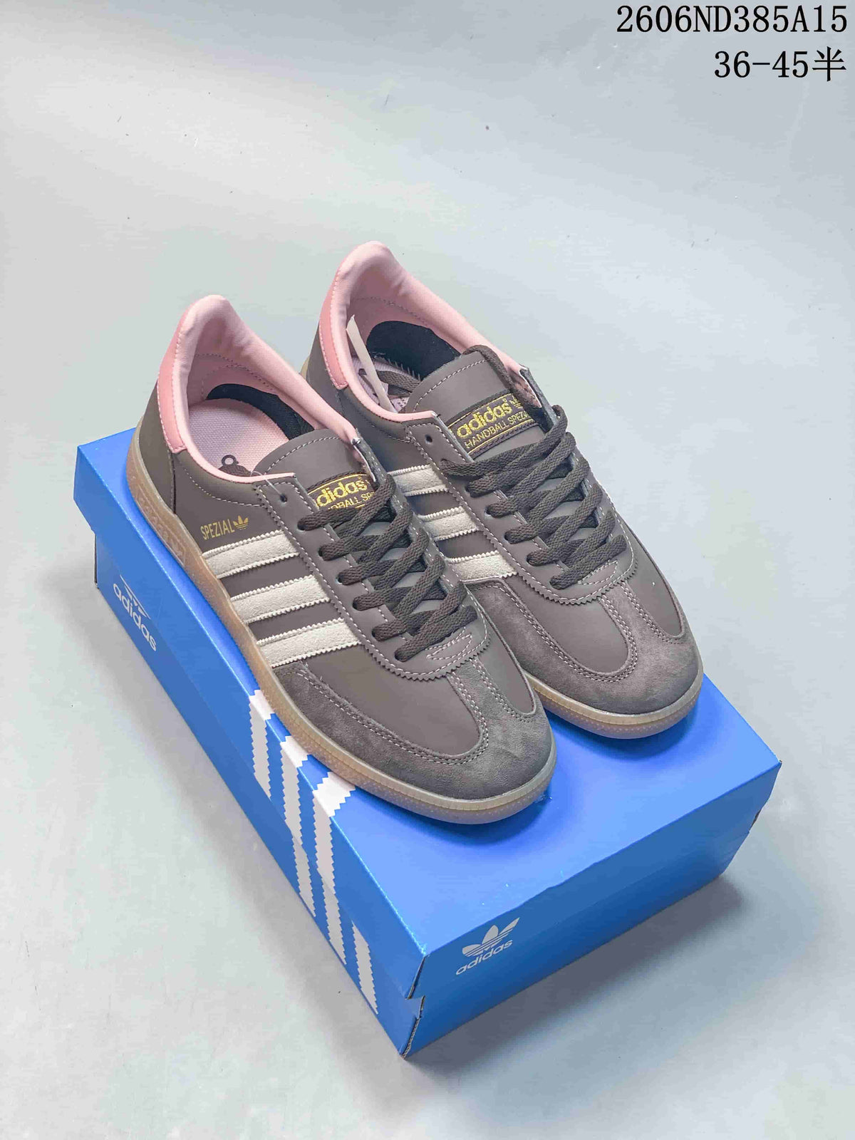 Pair of grey adidas Spezial sneakers with white stripes, pink accents and gum-colored soles, shown on a blue shoe box.