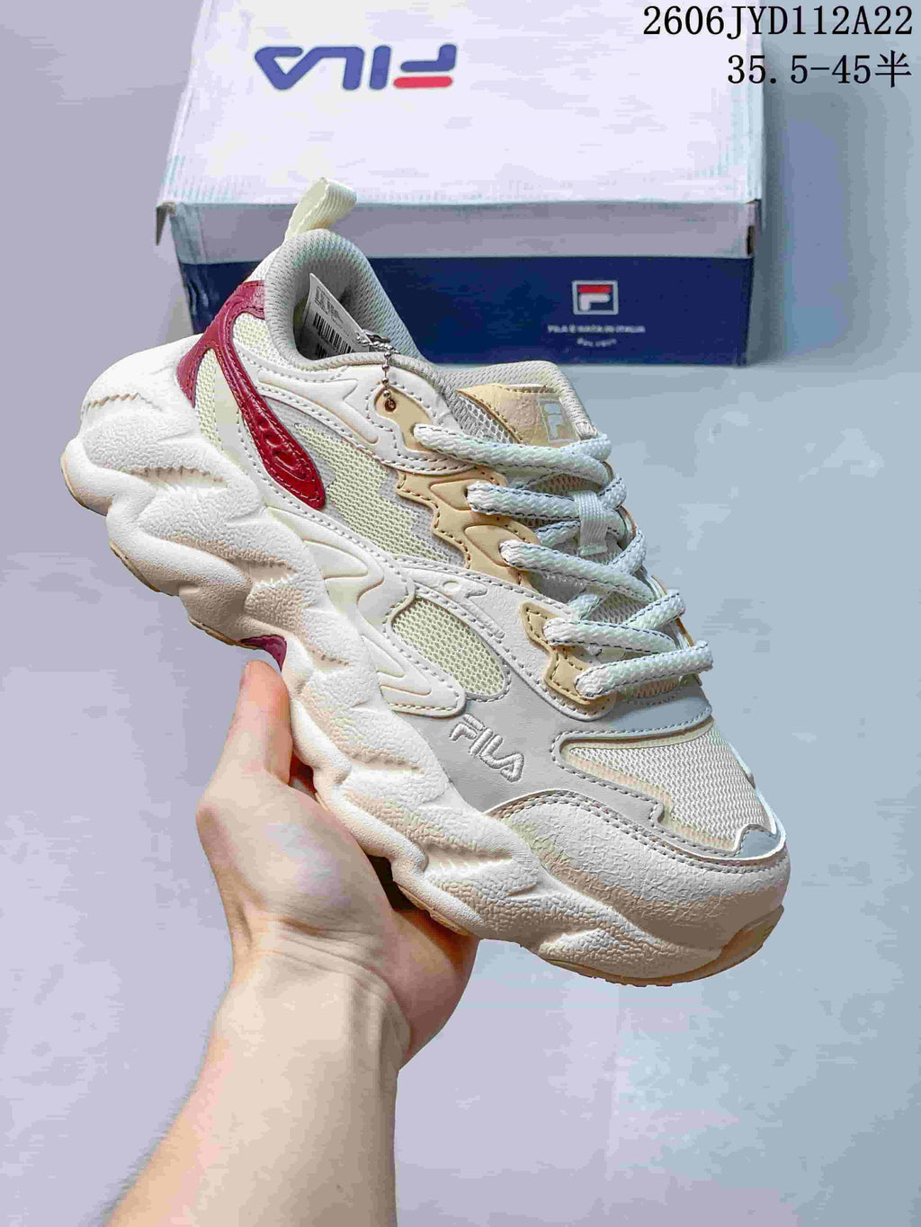 Close view of a cream FILA sneaker with red accents, mesh panels, and a chunky sole.